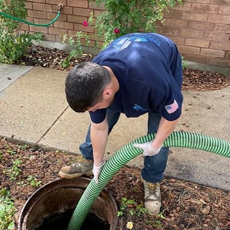 A plumber working with a large hose at an outdoor sewer or manhole opening.